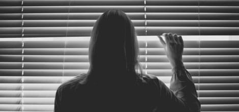 Woman looking through window blinds